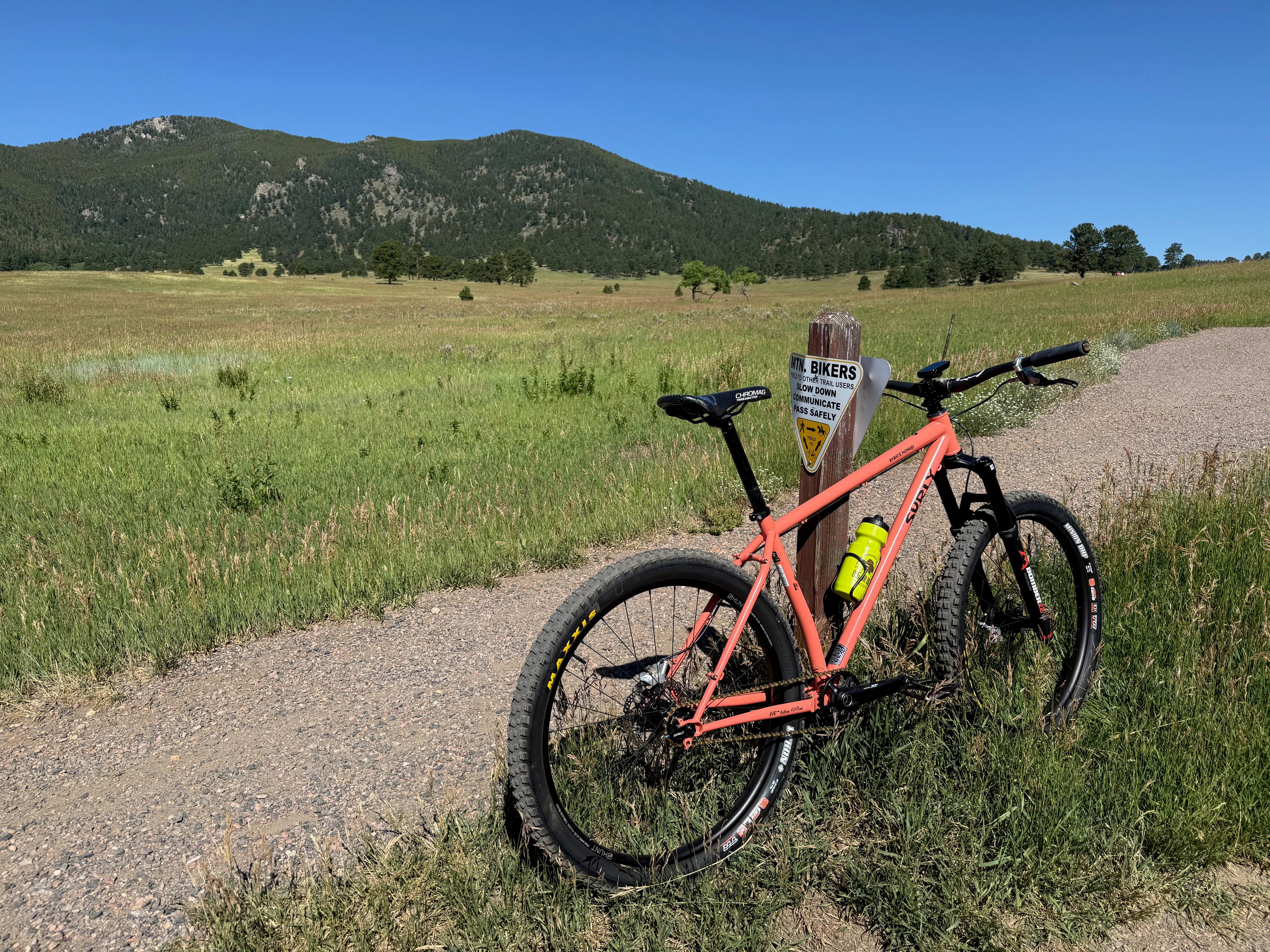 Salmon Surly Karate Monkey leaning against a trail sign post in a mountain meadow